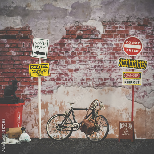 Bicycle. Vintage scene with bicycle parking between the street signs, red trash can and stay cats, brick wall background. Vintage with slight noise film grained filter. Soft focus on the leather bag.