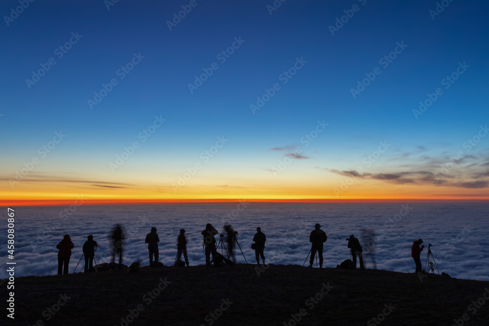 unfocused dark silhouettes of tourists photographers take pictures of the morning sunrise over the clouds