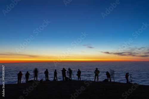 unfocused dark silhouettes of tourists photographers take pictures of the morning sunrise over the clouds