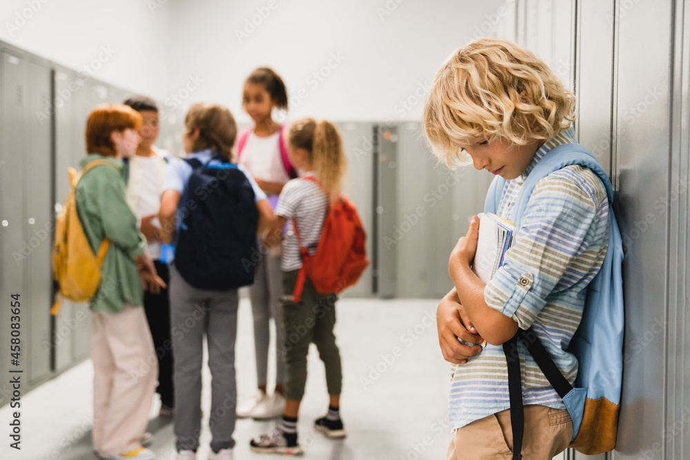 Lonely sad schoolboy crying while all his classmates ignoring him. Social exclusion problem. Bullying at school concept Lonely sad schoolboy crying while all his classmates ignoring him. Social exclusion problem. Bullying at school concept