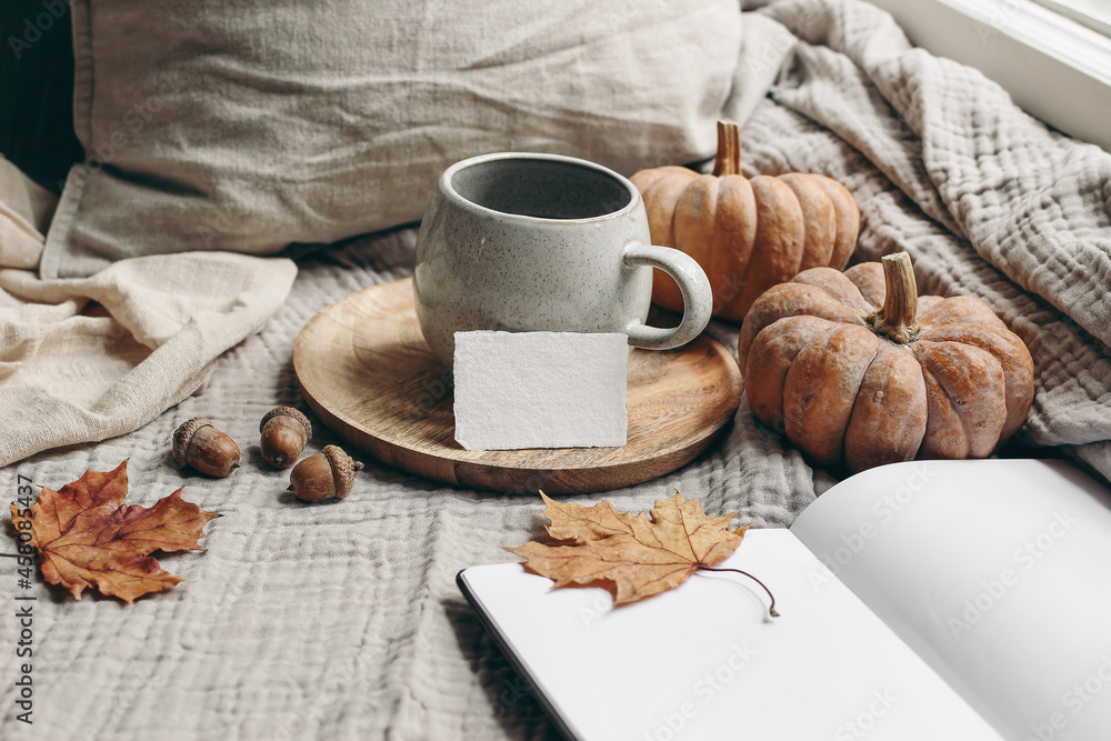 Cozy autumn morning breakfast still life. Cup of hot coffee, tea son wooden plate near window. Blank business card mockup. Fall, Thanksgiving concept. Orange pumpkins, acorns and maple leaves. - obrazy, fototapety, plakaty 