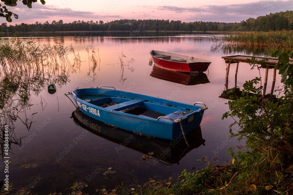 Small boats on a tranquil water of Rynskie lake (Jezioro Ryńskie) in Ryn, Poland. Masurian Lake District or Lakeland (Pojezierze Mazurskie or Mazury region).