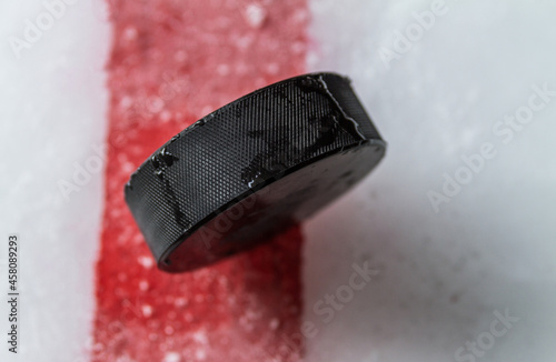 Photography Black hockey puck on the ice rink, with painted red line.