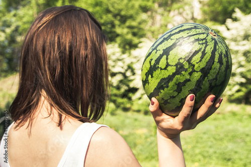 Young girl holding whole watermelon on a sunny summer day. 