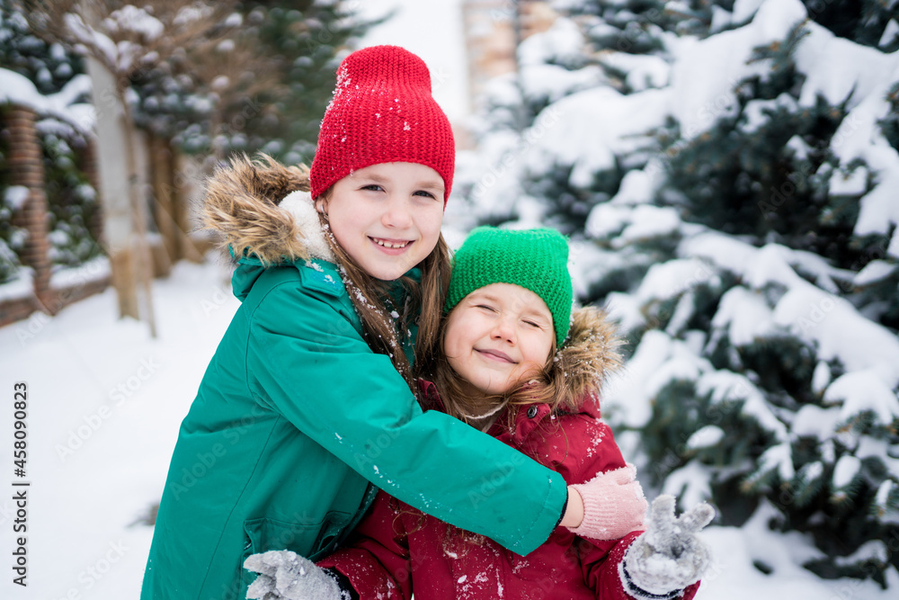 Winter portrait of two cute girls hugging each other. Children looking at the camera and smiling on a walk outside in snowy weather. Wintertime