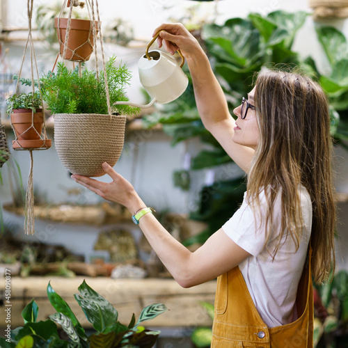 Photos Young female gardener watering potted plant handing