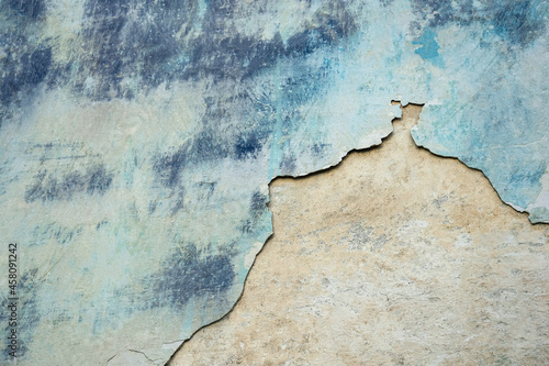 Wall of old building with partially fallen off plaster in gray and blue colors. Space is divided into two parts of different structures. Abstract background. Copy space. Close-up. Selective focus. © Marina_Nov