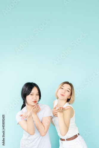 Sending love. Pretty female friends. Affection feelings. Tolerance acceptance. Happy asian caucasian women blowing kiss isolated blue. © golubovy
