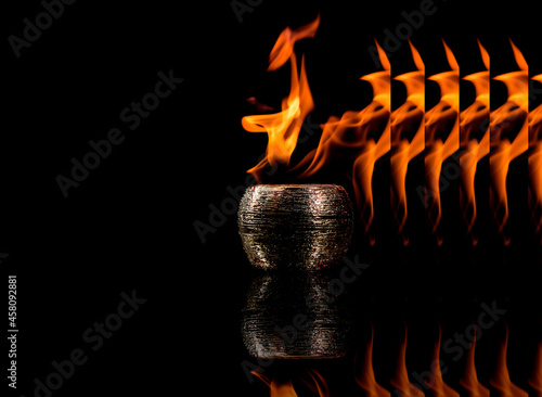 Pote dourado de cerâmica saindo sequencia de fogo de dentro em um fundo preto.  photo
