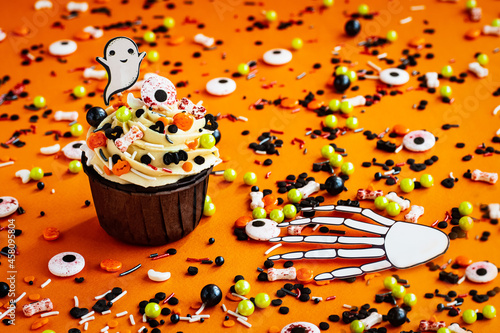 halloween cupcake ghost bone hand colored sprinkles on a colorful orange background photo