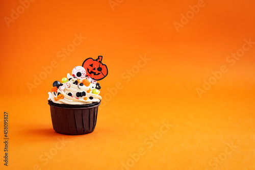 halloween cupcake decored with Jack O'Lantern colored sprinkles on a colorful orange background photo