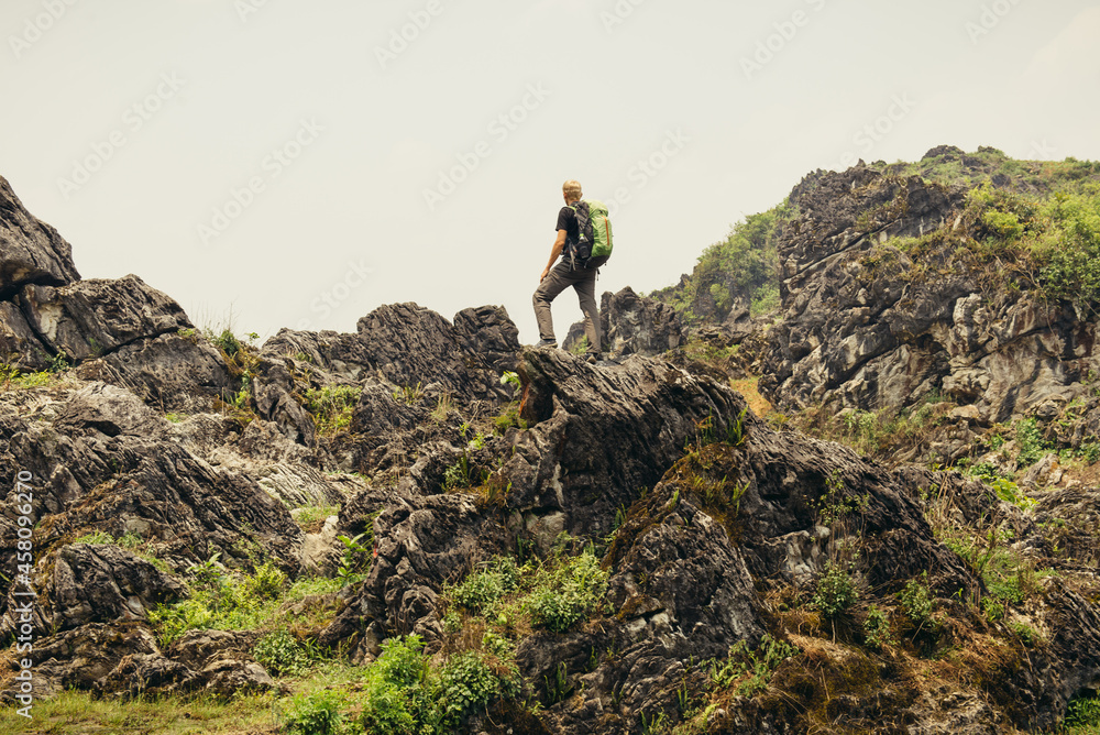Man hiking with backpack high in the green mountains in summer. Landscape observation during a short break. Copy space on the clear sky in Vietnam Man hiking with backpack high in the green mountains in summer. Landscape observation during a short break. Copy space on the clear sky in Vietnam