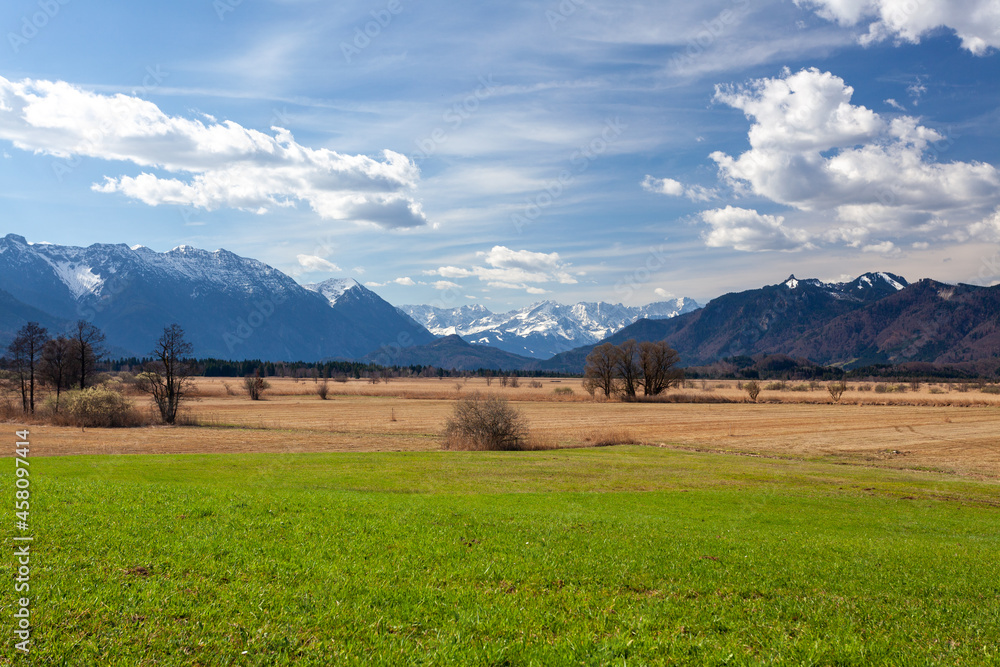 Spring panorama of green alpine meadows with snow-capped mountains 