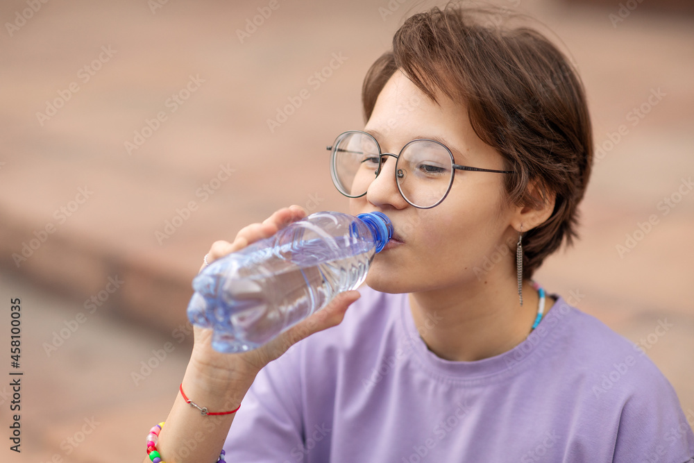 a brunette teenage girl with glasses on the streets of the city drinks water from a bottle on a clear sunny day a brunette teenage girl with glasses on the streets of the city drinks water from a bottle on a clear sunny day