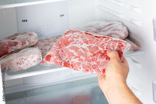 The Man takes out a bag of frozen meat from the freezer in the kitchen at home. photo