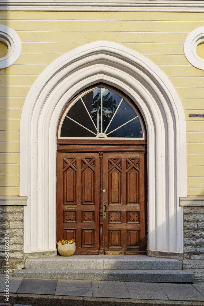 Wooden door over white stone arch and flower pot.
