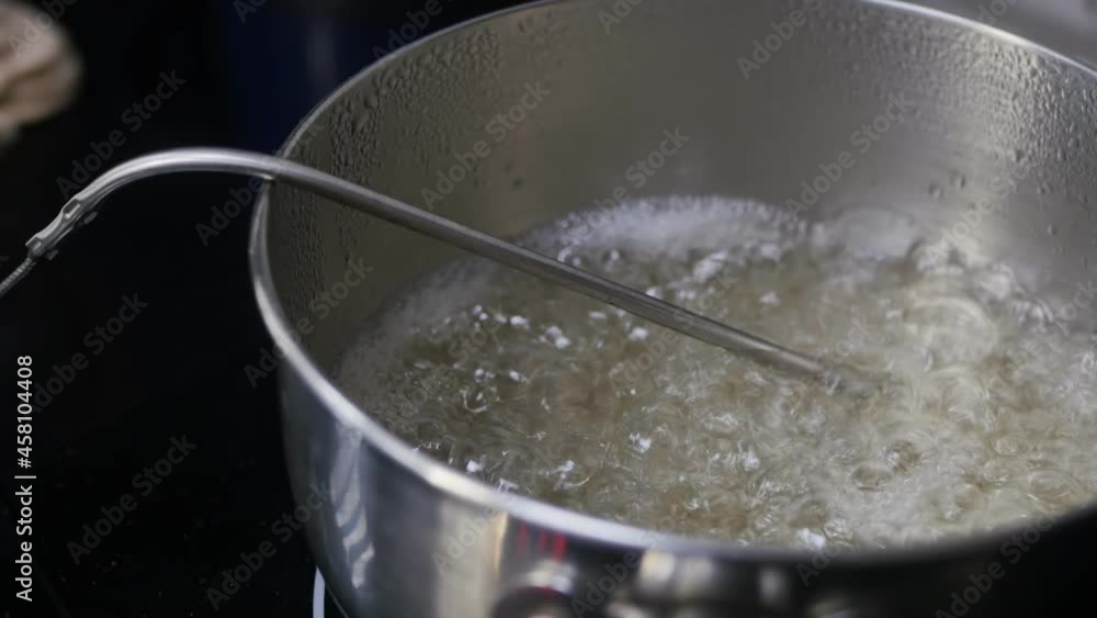 boiling sugar syrup in a metal saucepan on the stove with a thermometer probe