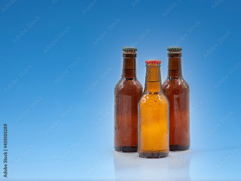 Three transparent brown beer bottles with water drops and cap on a blue background