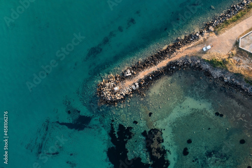 Top-down aerial view of a pier made of large stones going into the sea with clear turquoise water © Igor