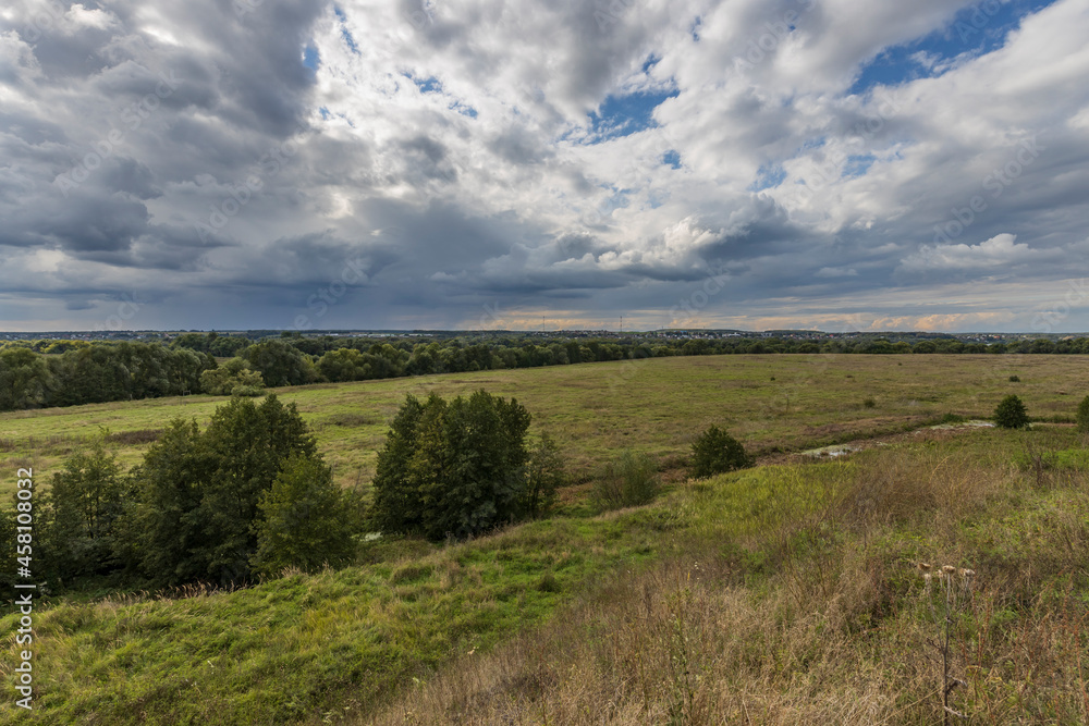 Obraz premium Summer field and clouds on the blue sky. A landscape with a bright green field and dramatic clouds against a blue sky.