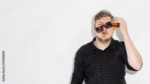 Party hangover. Alcohol problem. Drinking habit. After celebration. Messy man in sunglasses headache suffering with glass against head isolated on white empty space background. photo