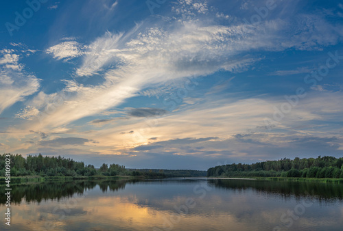 A picturesque landscape with a sunset sky reflected in a pond. Forest on the horizon. Sunset over the lake. © Sergei
