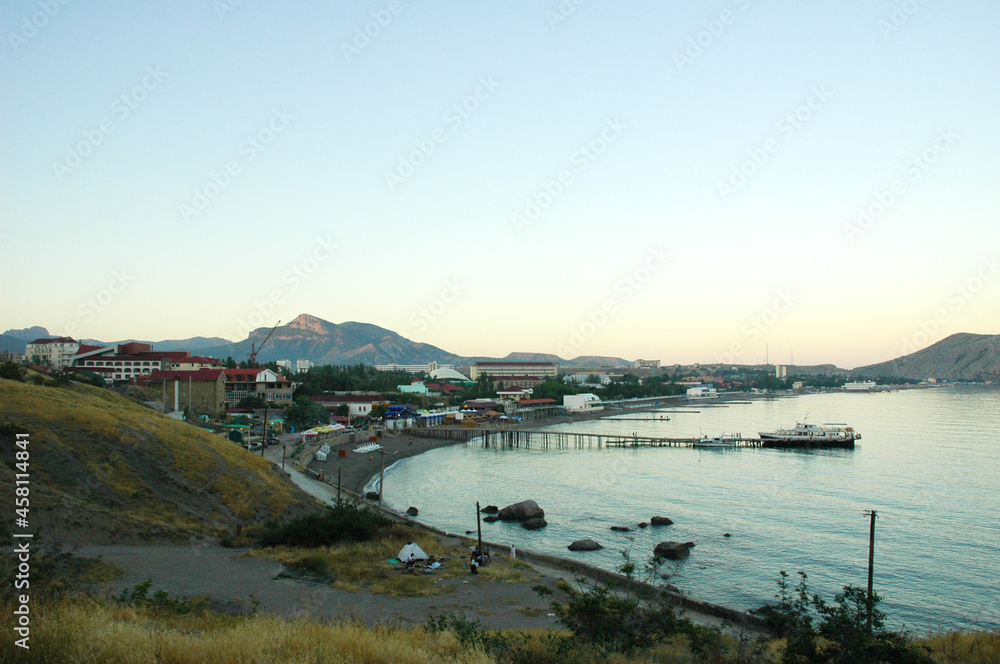 View of the pier in the city of Sudak. The boat docked at the pier at sunset. A bird's-eye view of the embankment. Crimea.