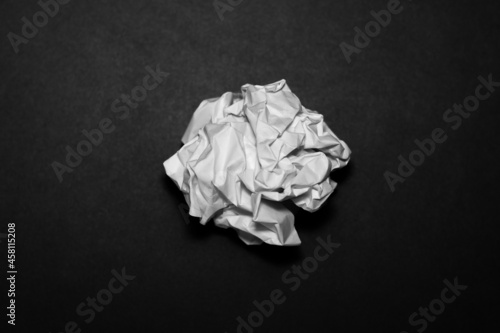 Close up of wadded up paper ball, crumpled ball of white paper isolated on black background, discarded trash paper