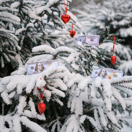 Christmas toys and money in us dollars hang on a snowy christmas tree