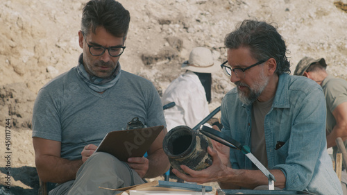 Male archaeologist showing vase to colleagues photo