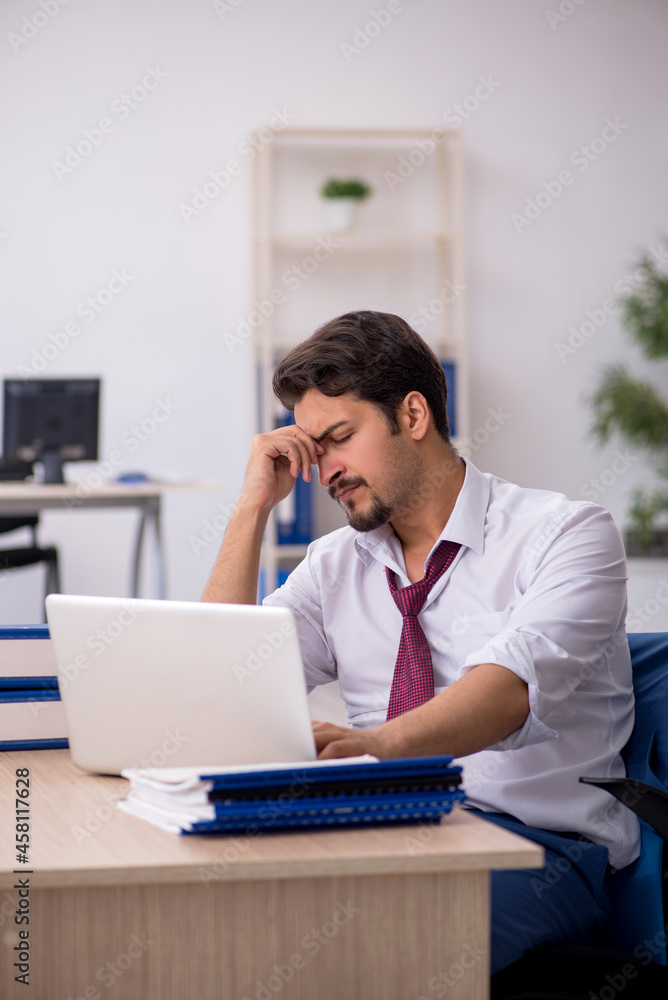 Young male employee unhappy with excessive work in the office Young male employee unhappy with excessive work in the office