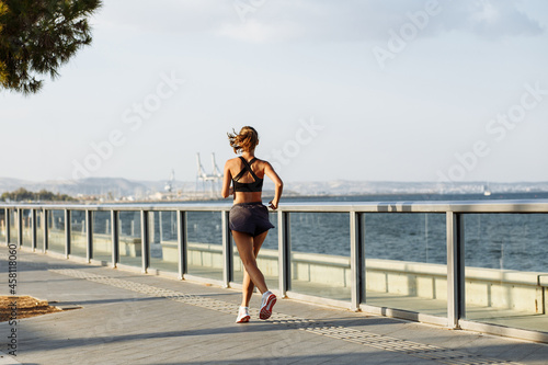beautiful fitness girl in shorts and sports top running on the waterfront by the sea in sunny weather © Taras