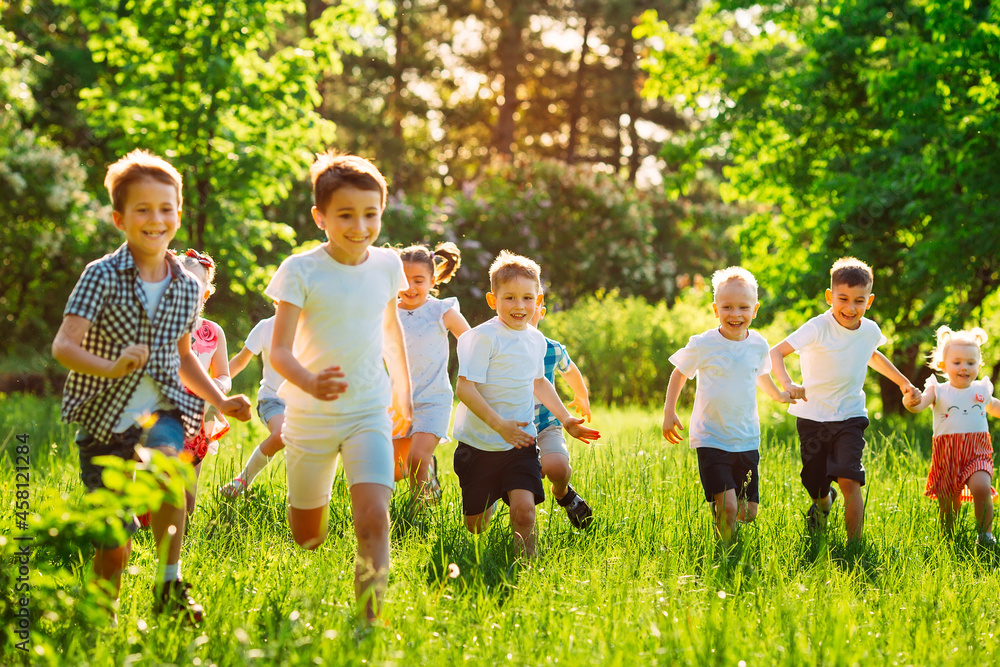 Obraz premium A group of happy children of boys and girls run in the Park on the grass on a Sunny summer day.