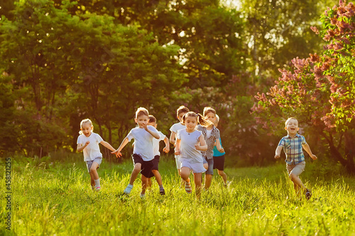 A group of happy children of boys and girls run in the Park on the grass on a Sunny summer day. © davit85