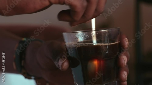 Photo of a person stirring sugar with a metal spoon in a glass of coffee