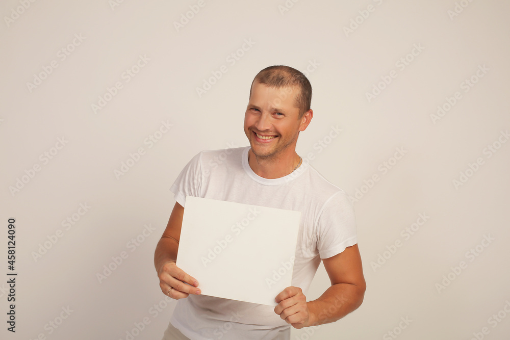 a young brutal guy in a white T-shirt holds a white sheet of paper in his hands a young brutal guy in a white T-shirt holds a white sheet of paper in his hands