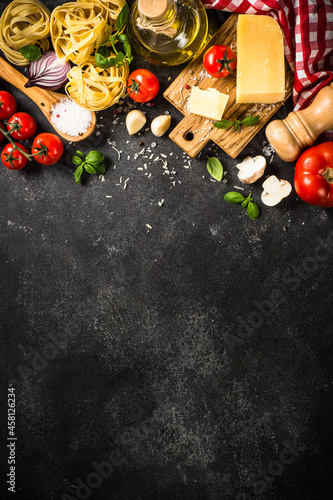 Italian food background. Raw Pasta, fresh tomatoes, olive oil, parmesan cheese, spices and basil on black stone table.