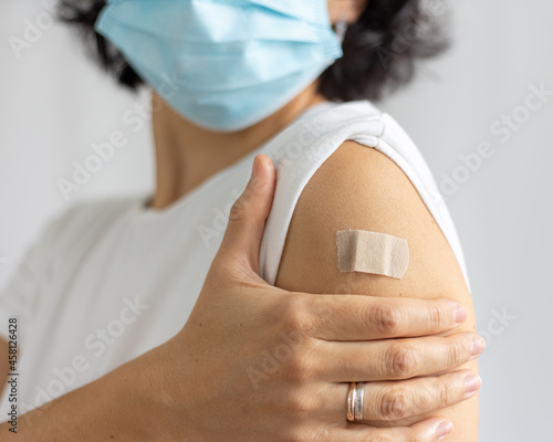 young woman in mask with plaster on her shoulder, after vaccination