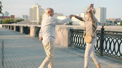 Happy senior man and woman are dancing in city street smiling enjoying romantic relationship on summer day. Happiness and family concept.