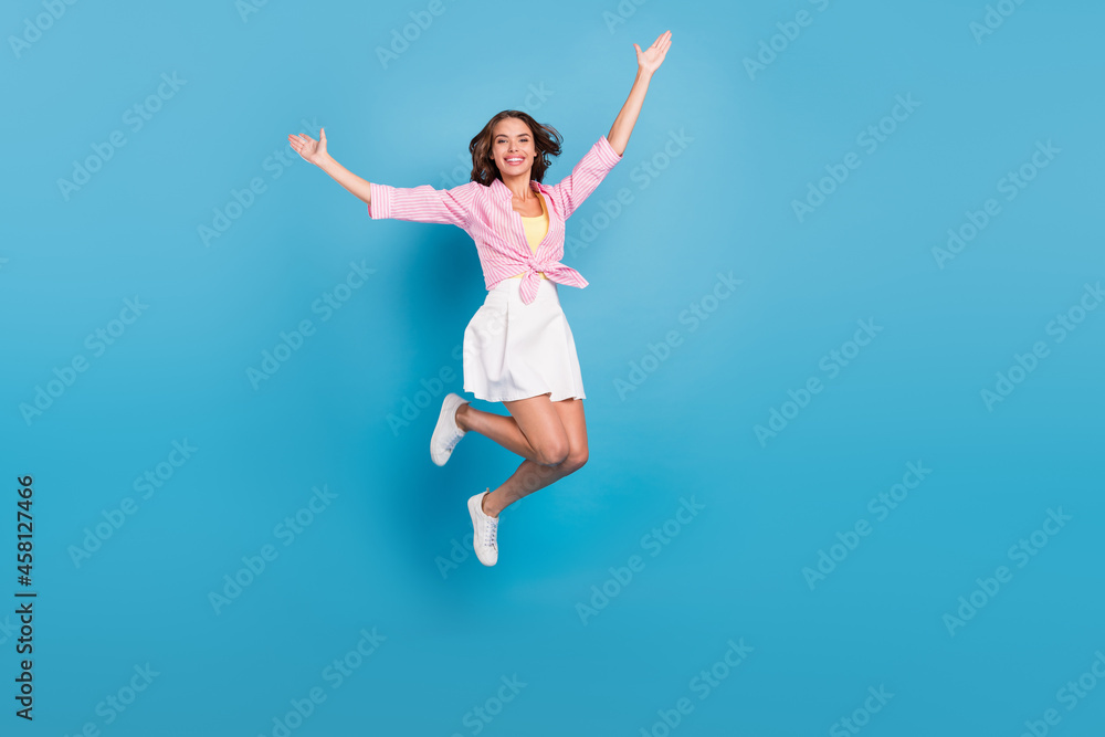 Photo of adorable shiny young woman dressed white skirt smiling rising hands arms jumping high isolated blue color background