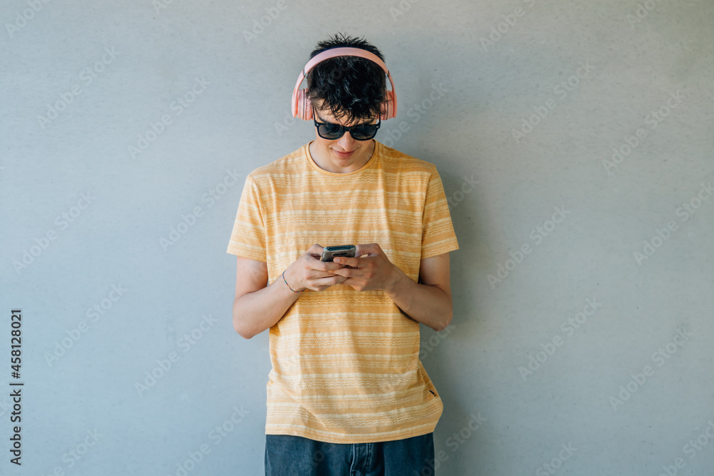 teenage boy with headphones and mobile phone on the wall teenage boy with headphones and mobile phone on the wall