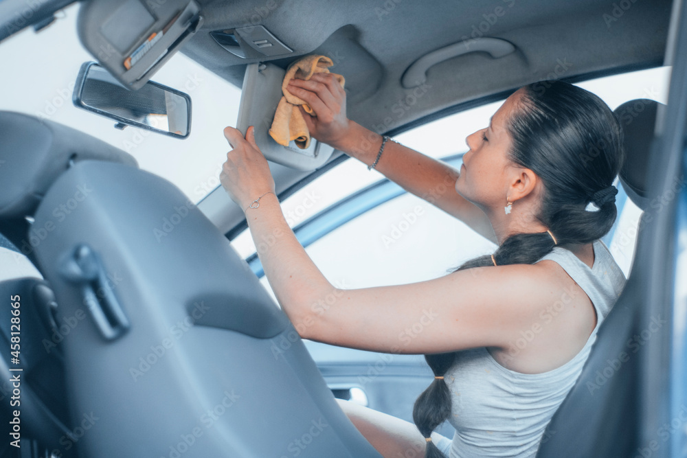 Mujer joven morena limpiando con un paño el interior del vehículo en el centro de lavado de coches de una gasolinera Mujer joven morena limpiando con un paño el interior del vehículo en el centro de lavado de coches de una gasolinera