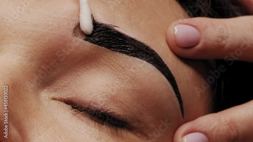 SLOW MOTION: Cosmetologist removes black eyebrow paint after coloring. Professional eyebrow coloring in black in a beauty salon. Working hands of the master close-up. Beauty treatment procedures photo