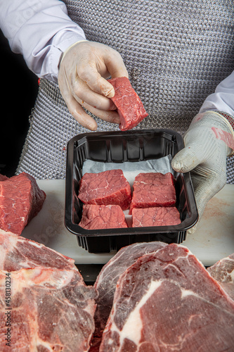 Butcher cutting beef. Chef in white latex gloves holding pieces of raw beef on a white polyurethane cutting board, on a dark background. photo