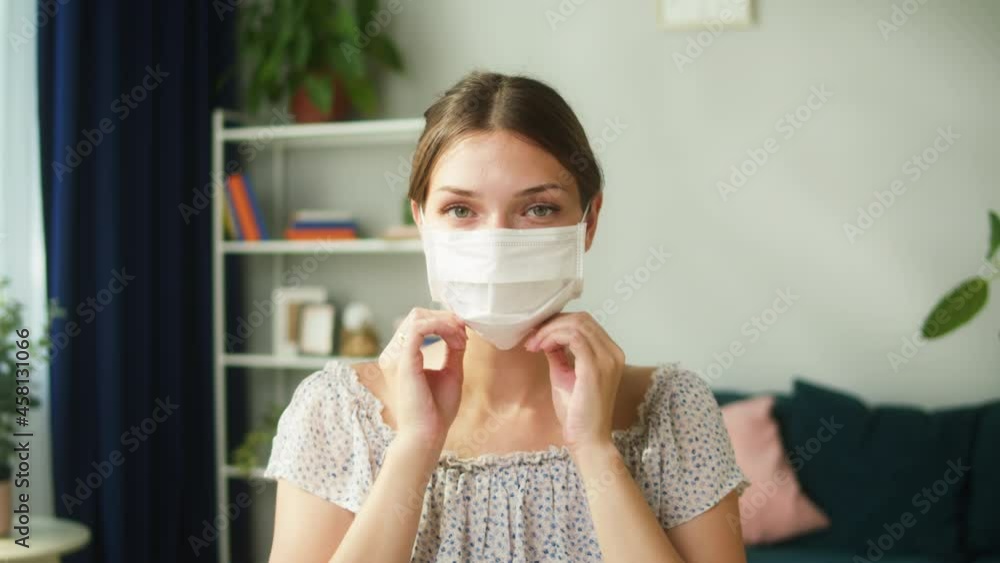 Young woman portrait. Female person wearing medical protective mask, looking in camera. Model posing in living room at home. Coronavirus lockdown isolation concept. Young woman portrait. Female person wearing medical protective mask, looking in camera. Model posing in living room at home. Coronavirus lockdown isolation concept.