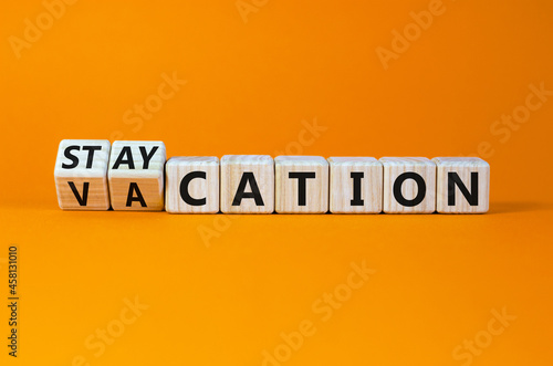 Vacation or staycation symbol. Turned wooden cubes and changed the word vacation to staycation. Business and vacation or staycation concept. Beautiful orange background, copy space. photo