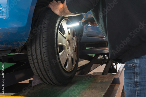 Workshop car inspection, checking with a flashlight the malformations of the wheel, suspensions and brakes, annual technical inspection of the vehicle