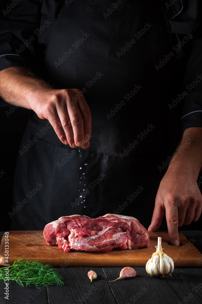 Chef sprinkles the meat with salt. Preparing meat before baking. Working environment in the kitchen of a restaurant