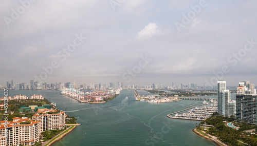 Incredible aerial view over the Miami shipping channels with the skyline on the horizon beyond and cloudy sky above as boats and ferries make their way to and from Fisher Island below. © Joseph Kirsch