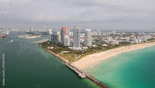 Incredible daytime aerial view of South Pointe high-rise condominiums looking down Miami Beach with sandy shores lining the turquoise waters of the Atlantic Ocean with cloudy sky above.